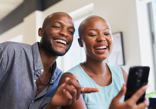 Two business owners smile as they review life and funeral cover options for employees on a phone. A man and women smile as they search for and review life and funeral insurance options via a phone.